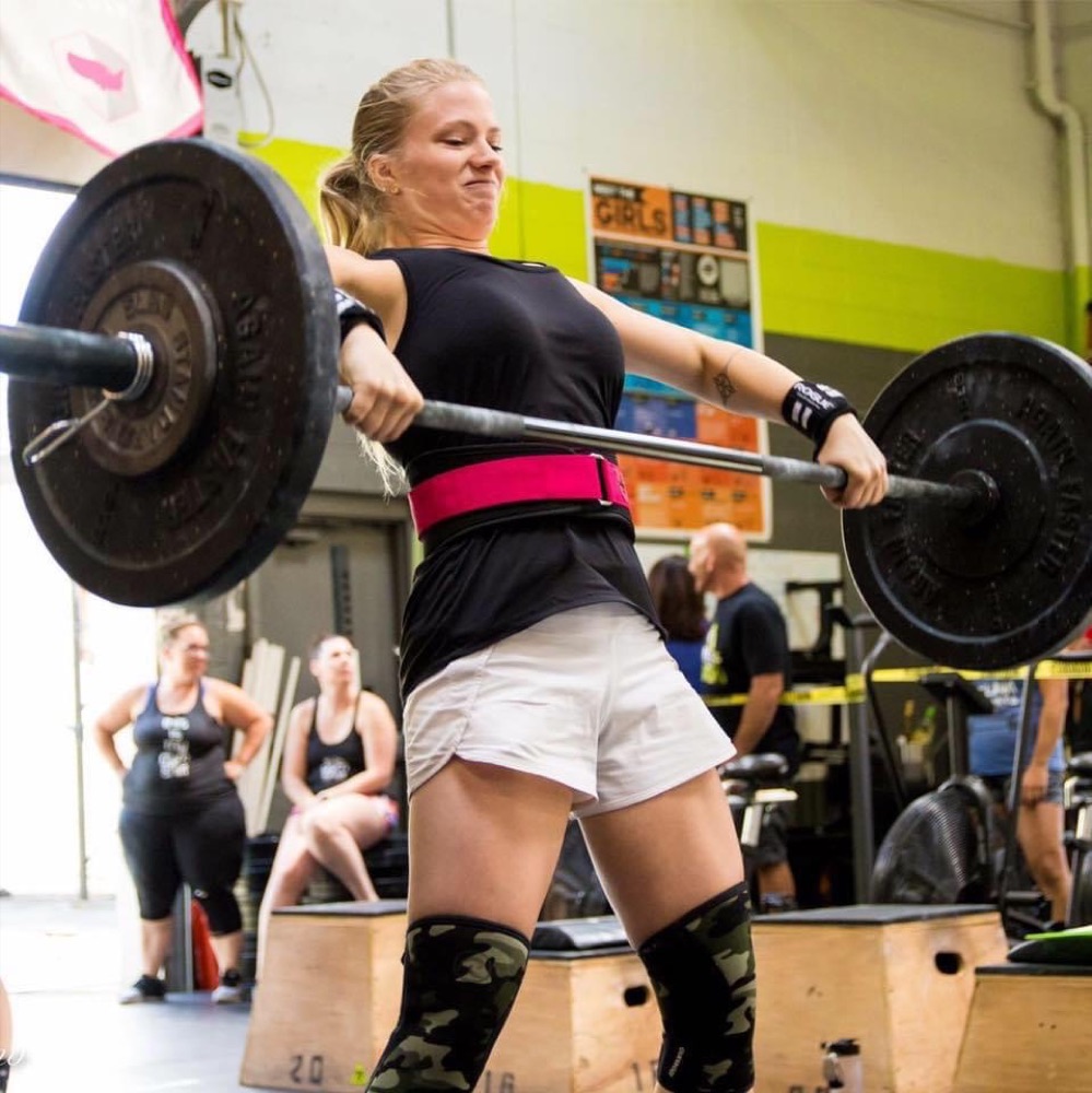 Beth mid-lift with a loaded barbell at the gym, pink belt on
