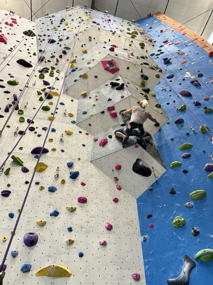 Beth high on a colorful indoor climbing wall