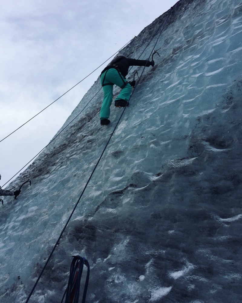 Beth ice climbing up a glacier wall on ropes in Iceland